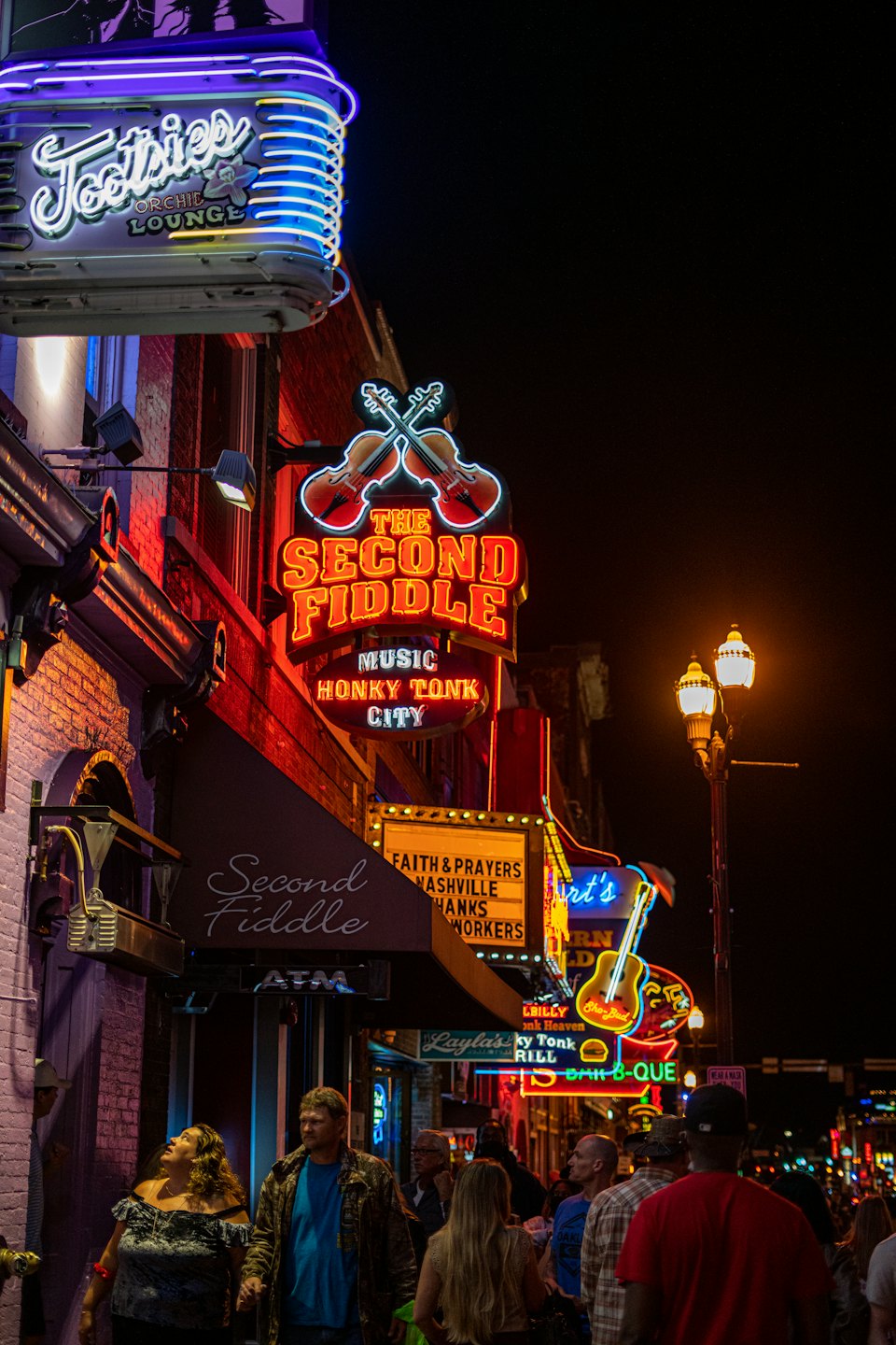 People walk down a neon-lit city street at night.