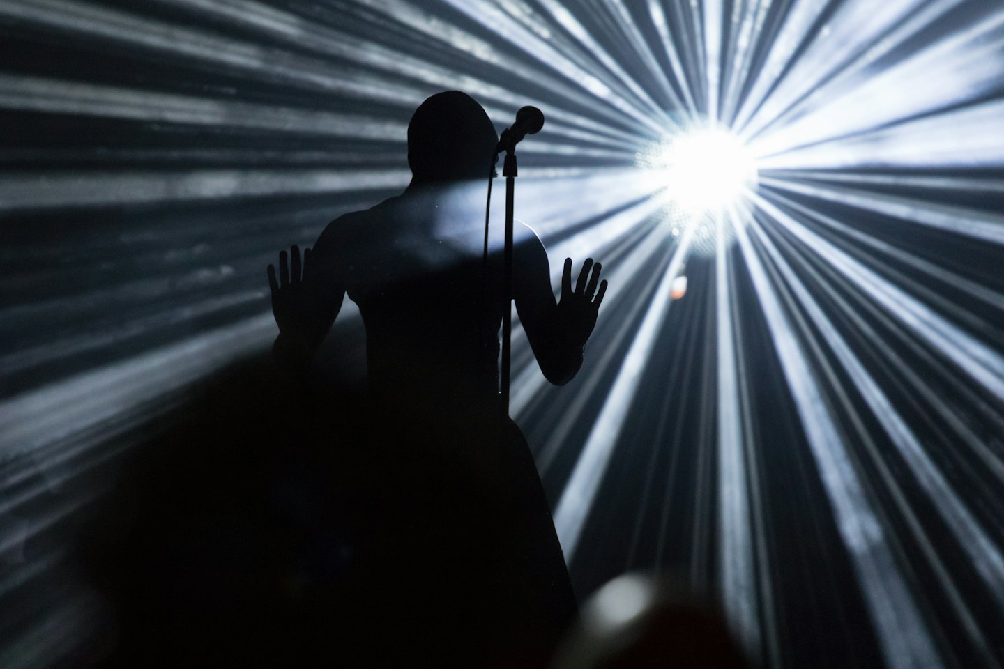 Performer silhouetted on stage with raised hands and microphone.