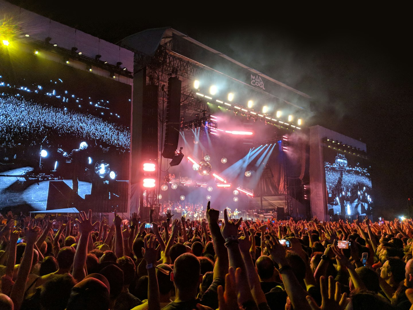 Concert crowd raising hands toward a stage with disco balls.