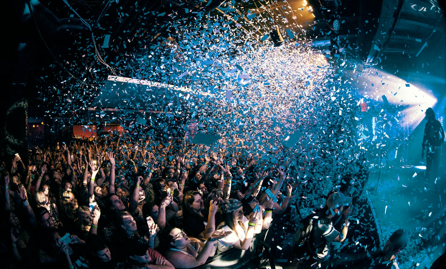 Audience cheers and raises hands at concert with confetti falling.